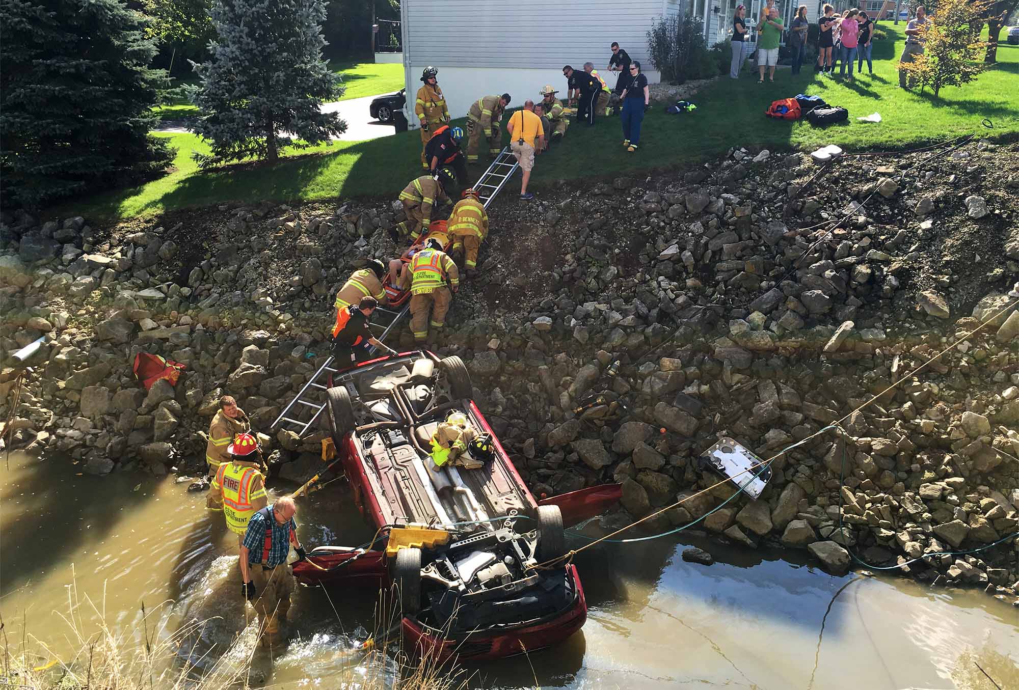 An unidentified man is slid up an embankment on a backboard after he was injured Tuesday afternoon when his car rolled down and overturned into Sucker Run Creek near W. Maple Street just west of Race Street.